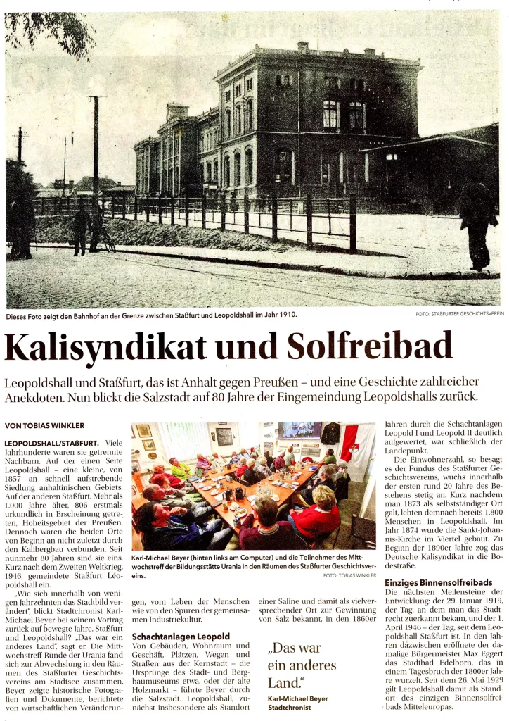 Eine historische Aufnahme des Bahnhofs in Staßfurt mit Personen davor. Das Gebäude ist mehrstöckig und hat eine klassische Architektur.