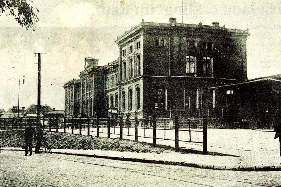 Eine historische Aufnahme des Bahnhofs in Staßfurt mit Personen davor. Das Gebäude ist mehrstöckig und hat eine klassische Architektur.