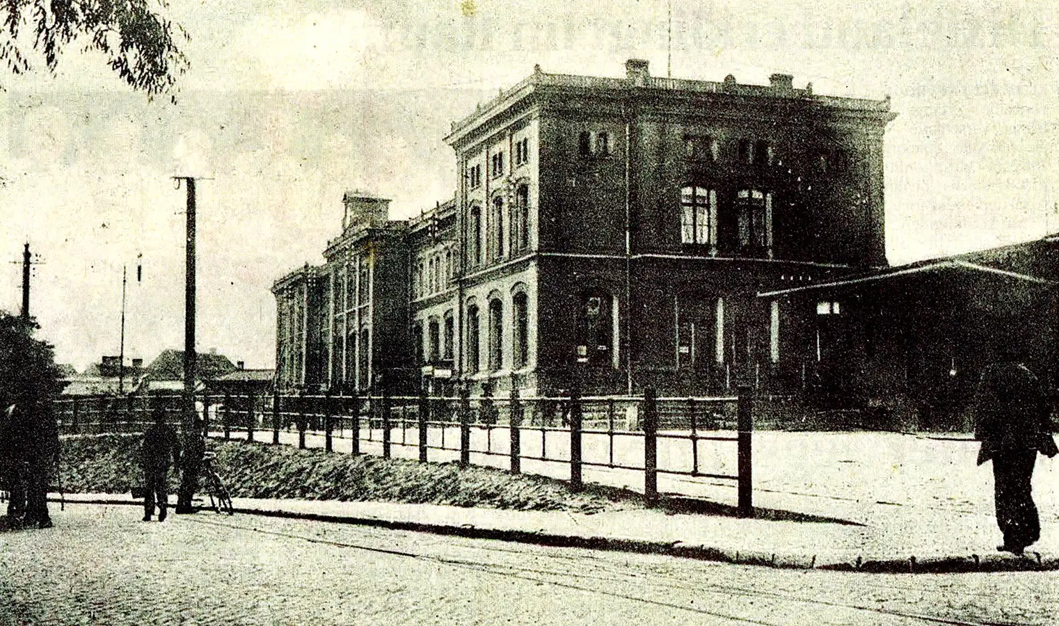 Eine historische Aufnahme des Bahnhofs in Staßfurt mit Personen davor. Das Gebäude ist mehrstöckig und hat eine klassische Architektur.